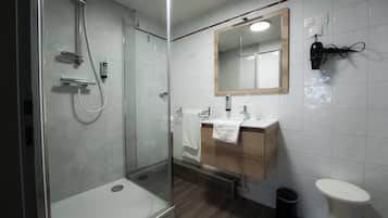 Un baño moderno con ducha envuelta en vidrio, tocador de madera, lavabo blanco y espejo.