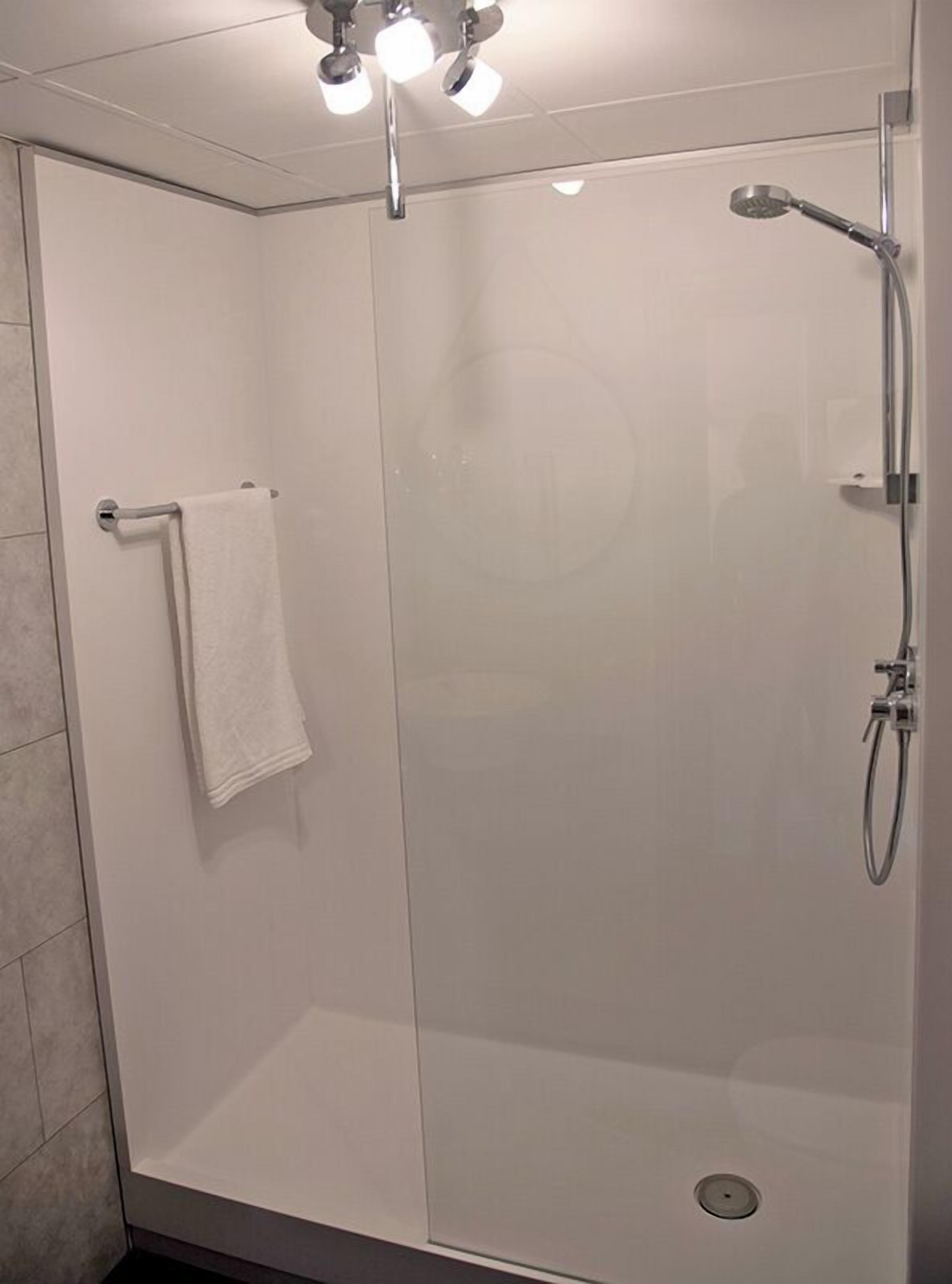 Una ducha moderna con puerta de vidrio, un perchero y un cabezal de ducha manual.