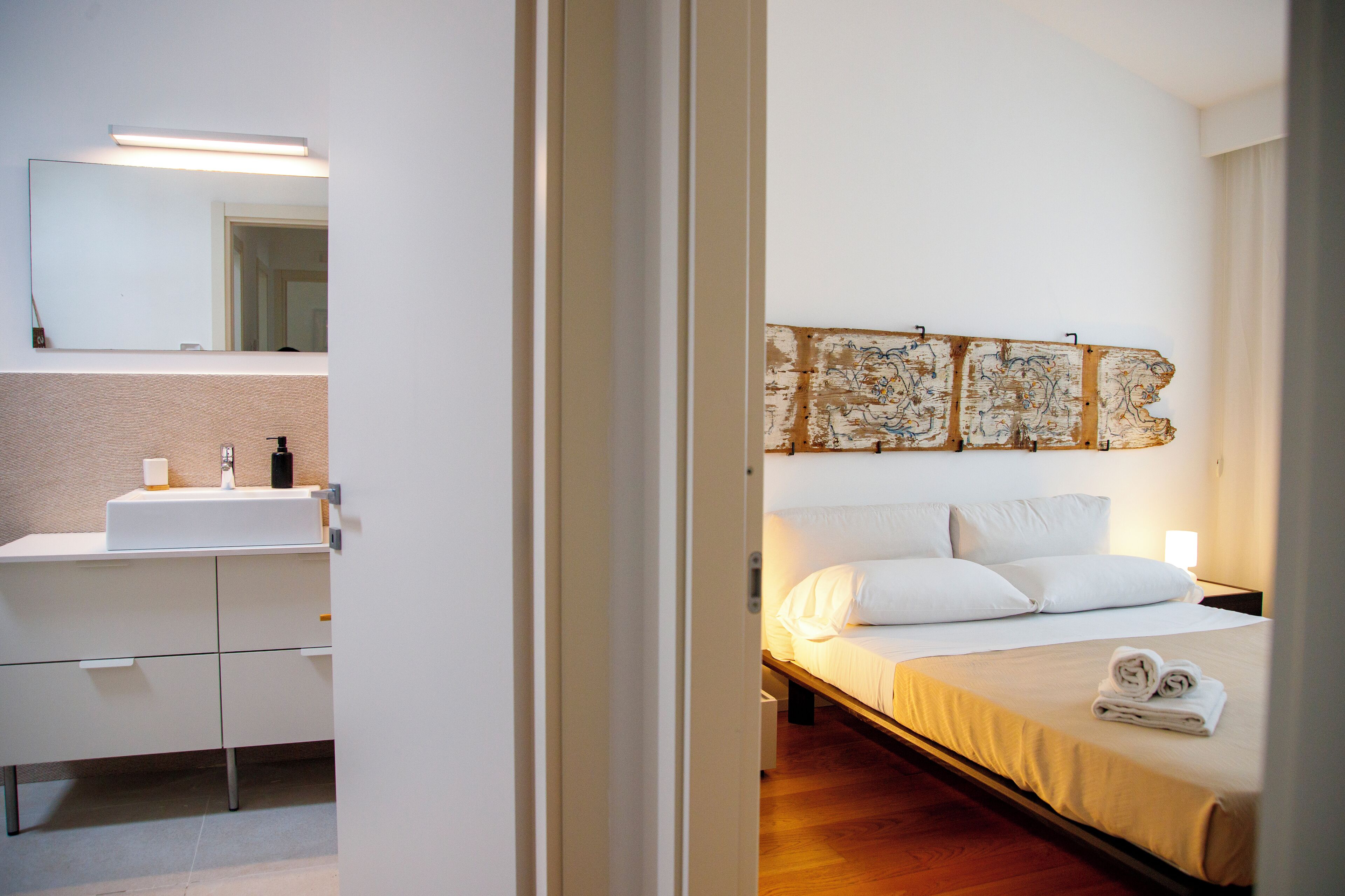 Habitación de hotel con lavamanos blanco, espejo y cama con ropa blanca.