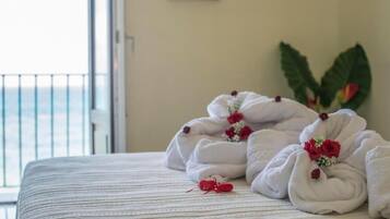 Una cama con toallas ordenadas y rosas rojas, una ventana con vistas y una planta en la pared.
