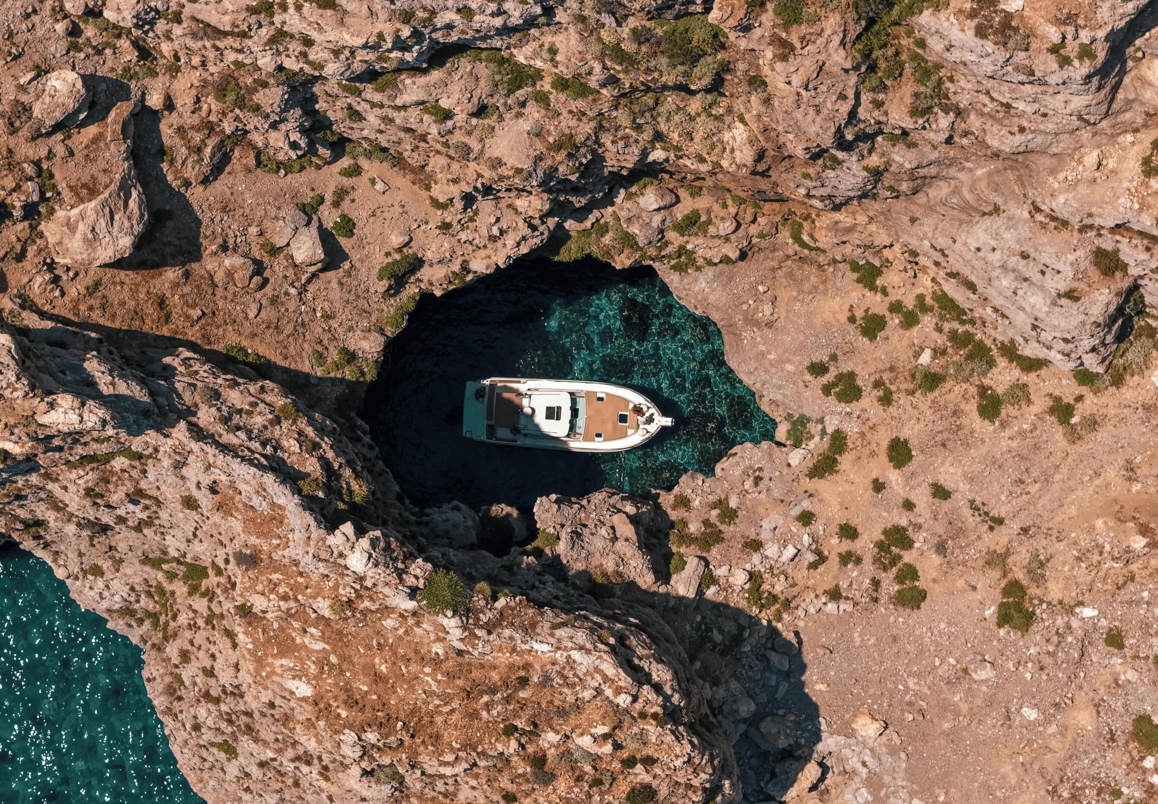 Vista aérea de un barco anclado en una cala rocosa con agua turquesa cristalina.