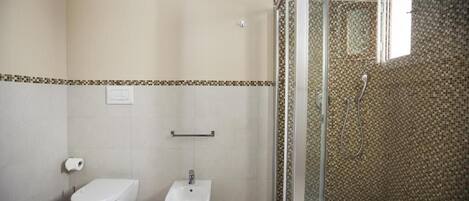 A bathroom with a toilet, bidet, and glass-enclosed shower area.