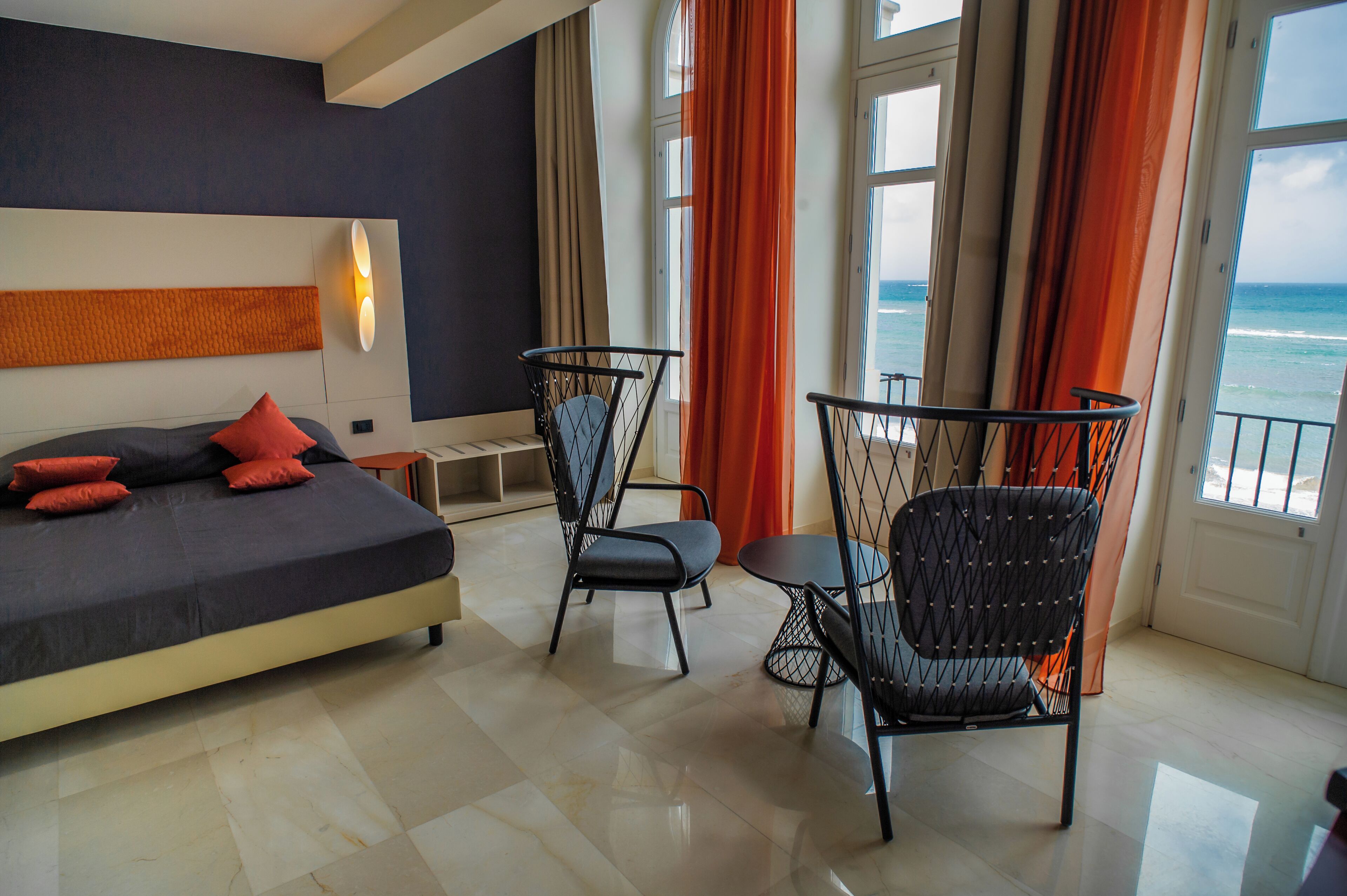 Una camera d'albergo moderna con un letto grande, due poltrone e vista sull'oceano tramite ampie finestre.