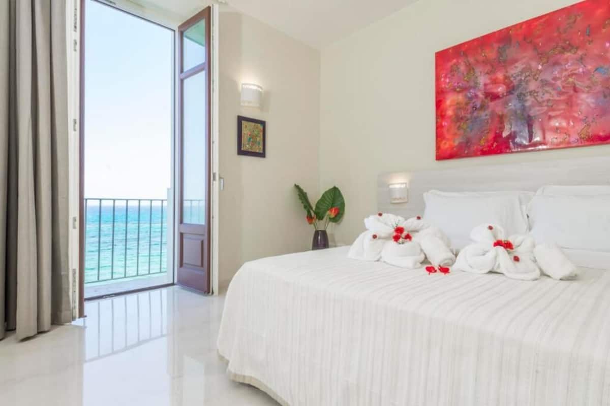 Habitación de hotel con cama, un cuadro, un jarrón con flores y vista al océano.