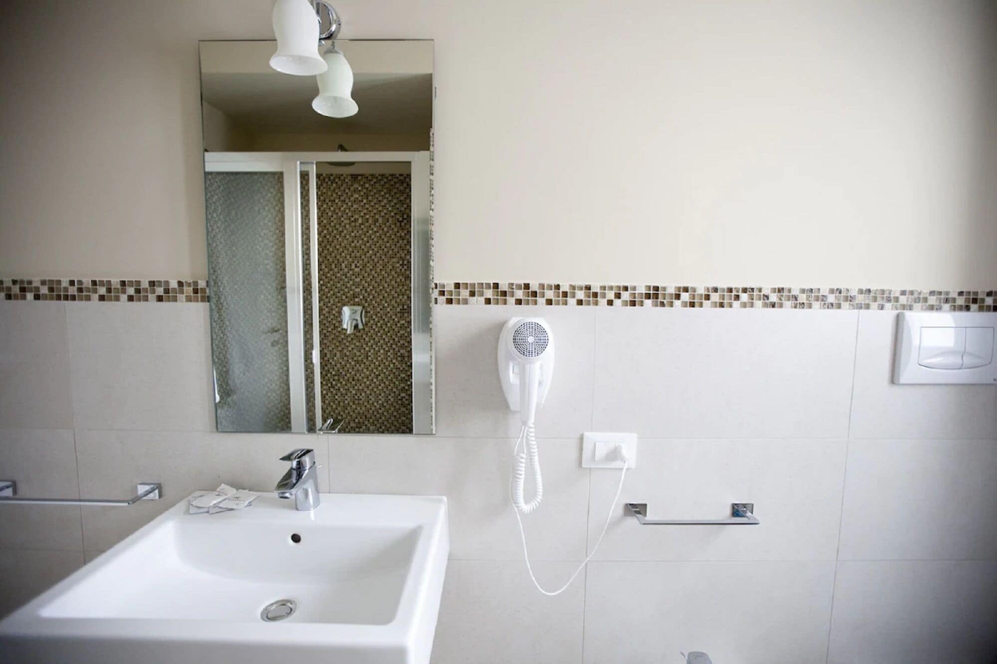 Un baño con lavamanos blanco, espejo, secador de pelo y toallero.