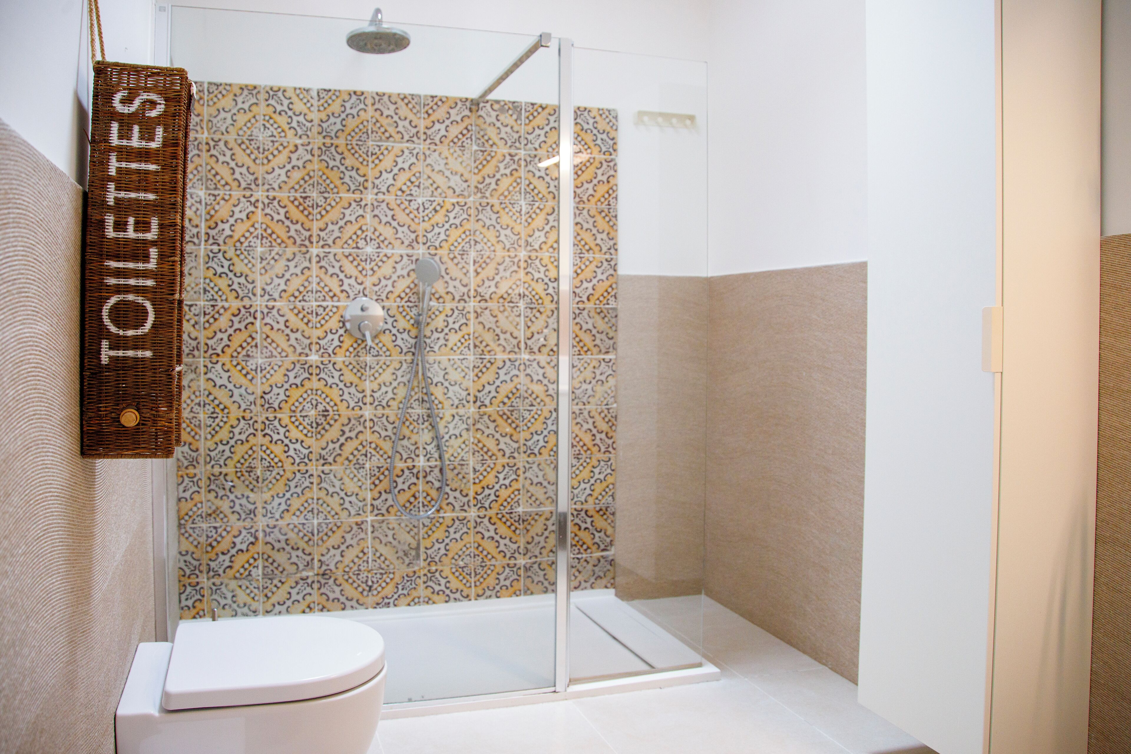 Une salle de bain avec douche, toilettes et un mur recouvert de carreaux décoratifs.