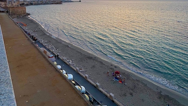 Un paisaje urbano costero con un paseo marítimo, playa y cielo despejado al atardecer.
