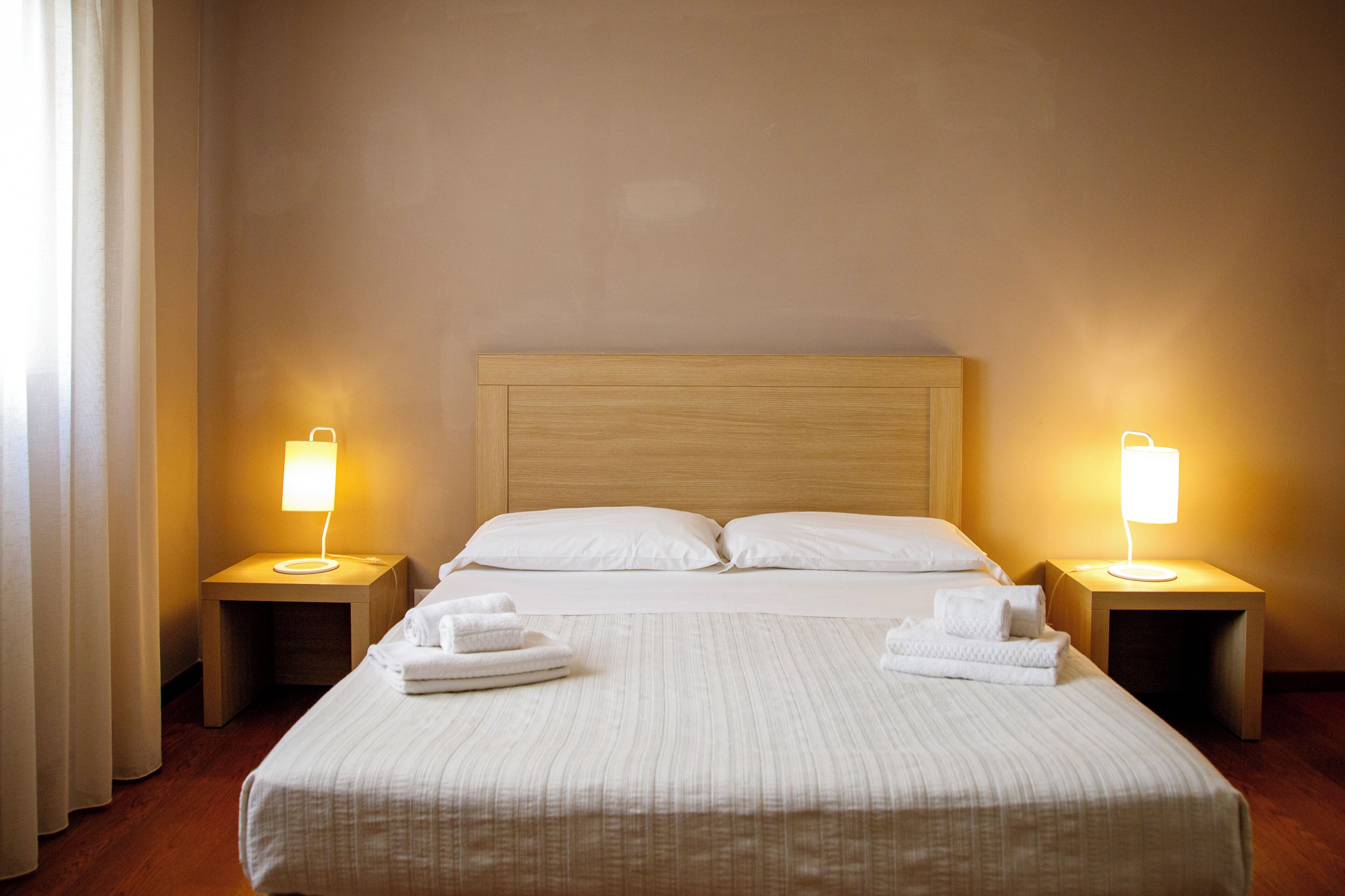 A neatly made bed with white linens and two bedside lamps on wooden nightstands.