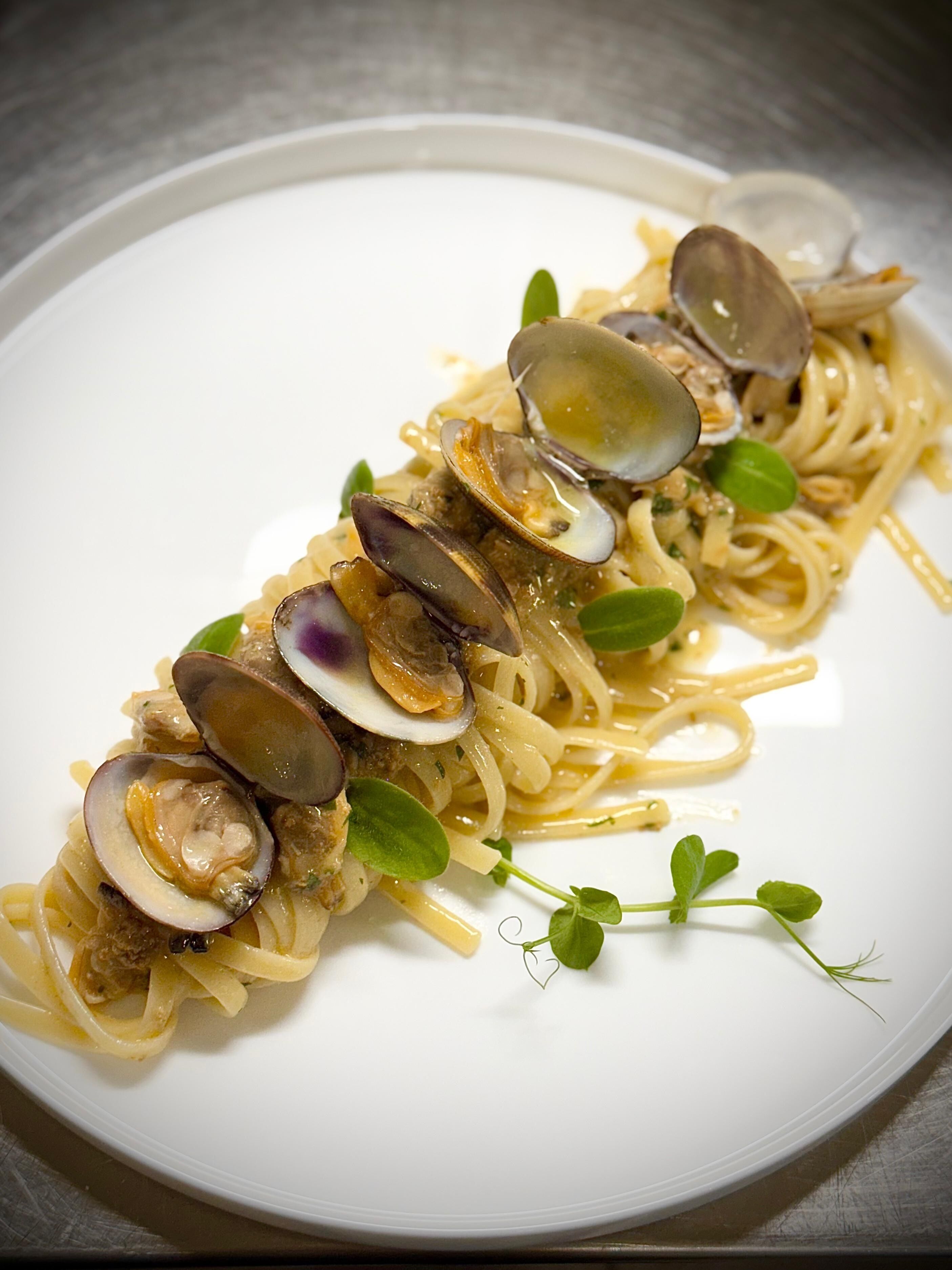 Un plat de spaghetti amb cloïsses i guarnició.