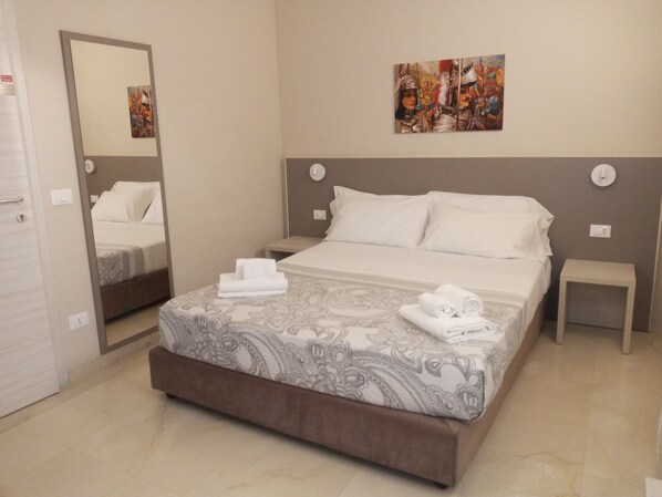 A hotel room with a large bed, a bedside table, a nightstand, a mirror, and a painting on the wall.