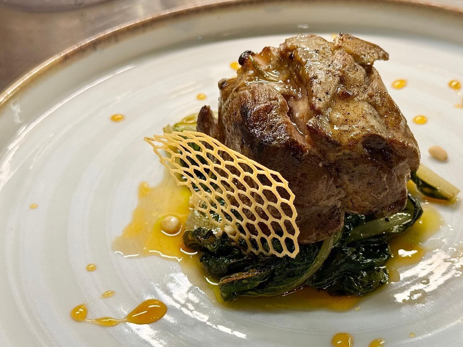 A plate with a piece of meat, greens, and a decorative element.