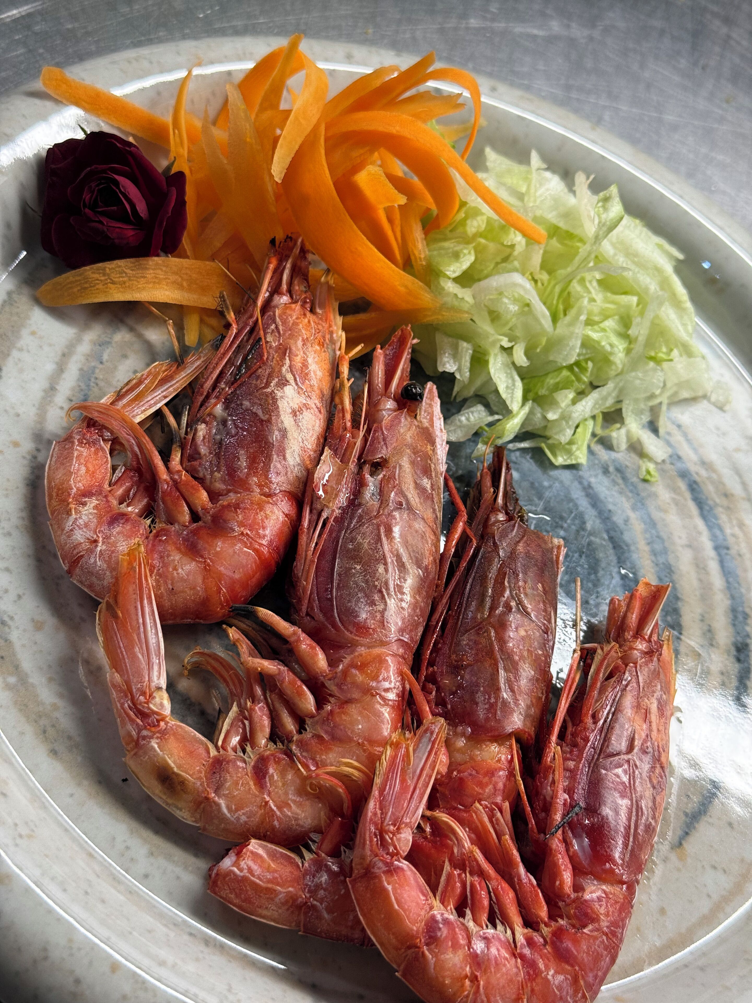 A plate with cooked shrimp, shredded carrots, and lettuce.