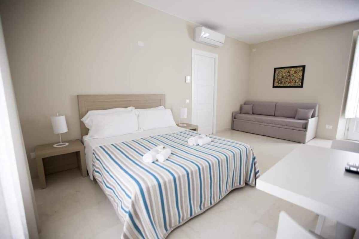 Una habitación de hotel con cama, mesita de noche, lámpara y sofá.