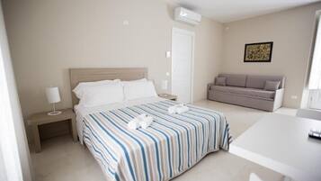 A hotel room with a bed, bedside table, lamp, and a sofa.