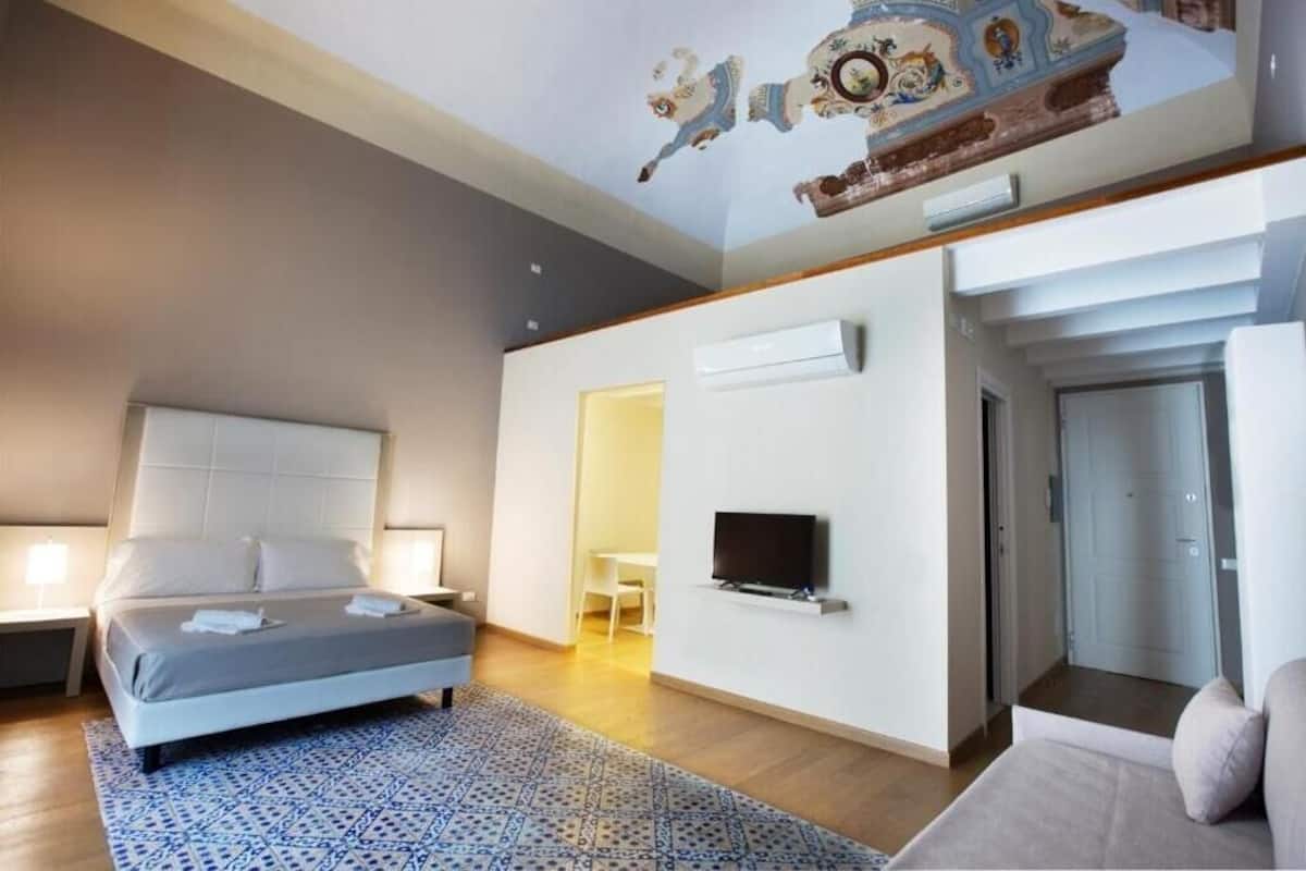 Una habitación de hotel moderna con una cama grande, un televisor de pantalla plana y un mural en el techo.