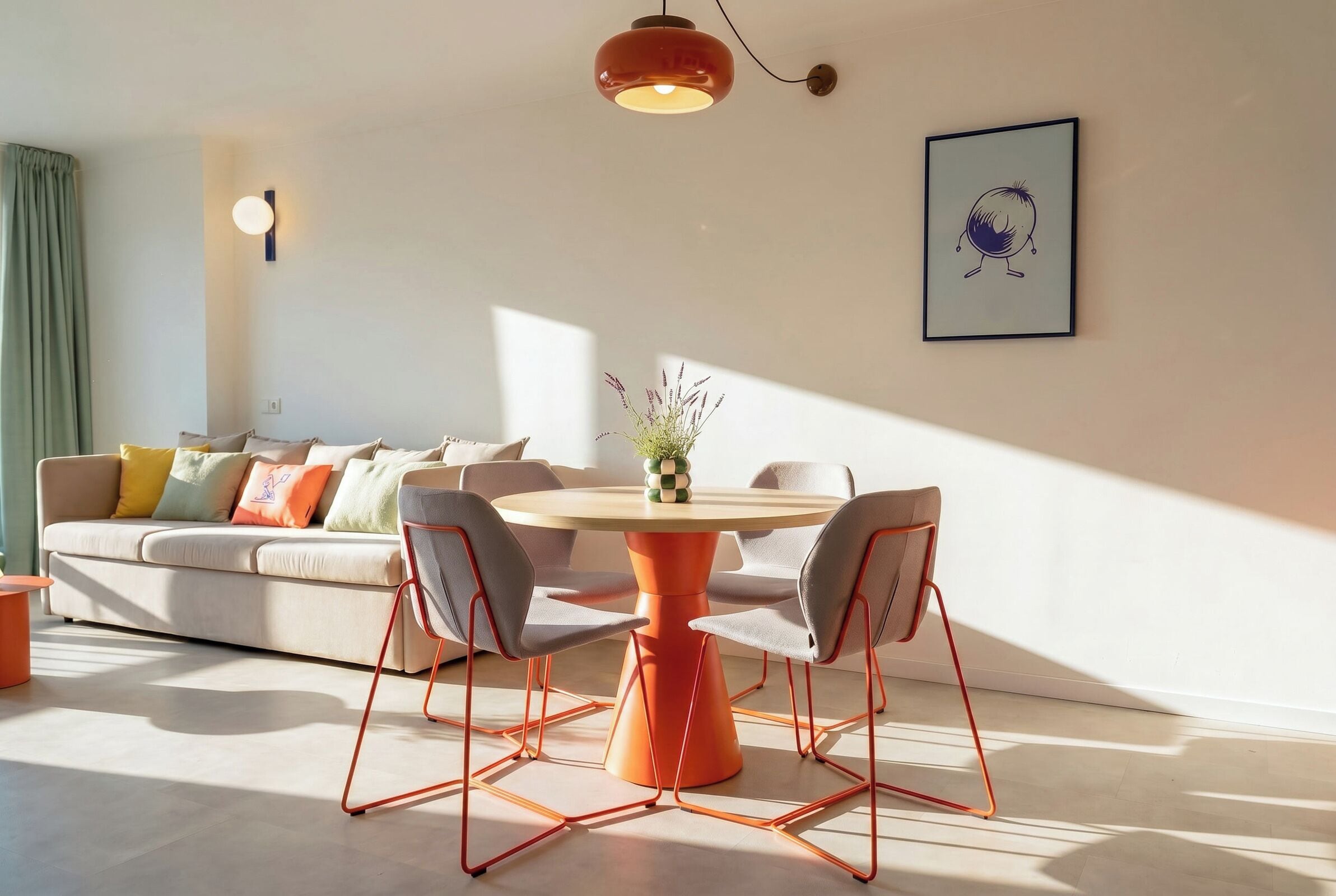 Una sala de estar moderna con una mesa redonda naranja, sillas grises, un sofá beige con cojines coloridos, una lámpara de pared e imagen enmarcada.