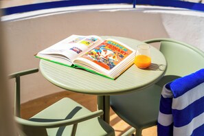 Une chaise verte, une petite table ronde, un livre et un verre de jus d’orange.