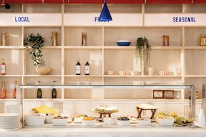 A buffet setup with labeled sections for local, fresh, and seasonal items, including wine bottles and various food dishes.