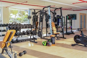 A gym with weightlifting equipment, dumbbells, a bench, and cardio machines.