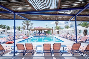 A poolside area with lounge chairs and umbrellas, a pool, and a covered seating area with tables. - Coral Star Hotel & Apartments (Sant Josep de sa Talaia)