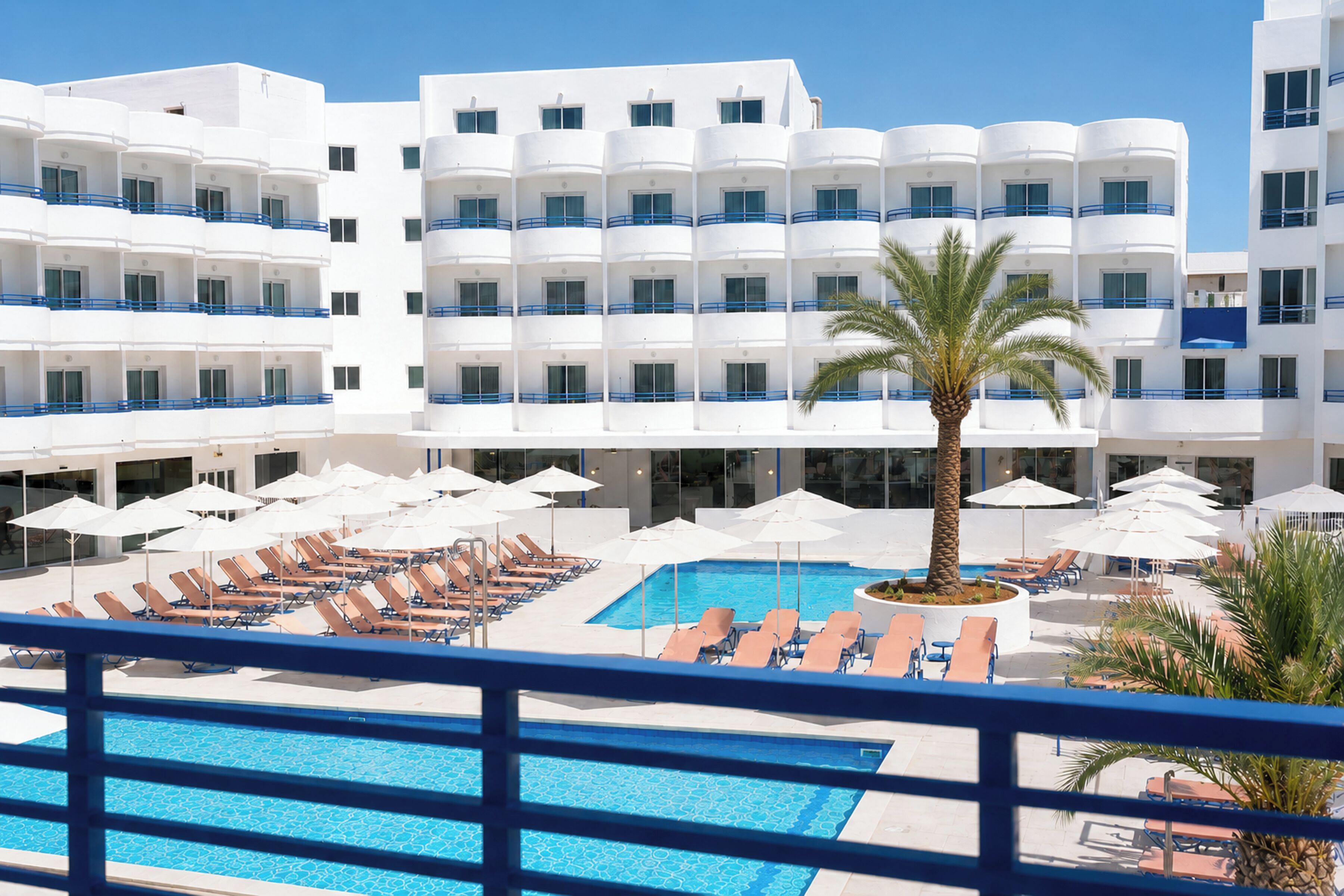 Ein Hotel mit mehreren Etagen, einem Schwimmbad, Liegestühlen und Sonnenschirmen.