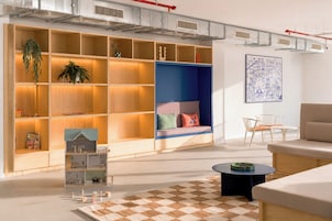 A modern living room with a large wooden bookshelf, a blue seating area, a white sofa, a round coffee table, and a checkered rug.