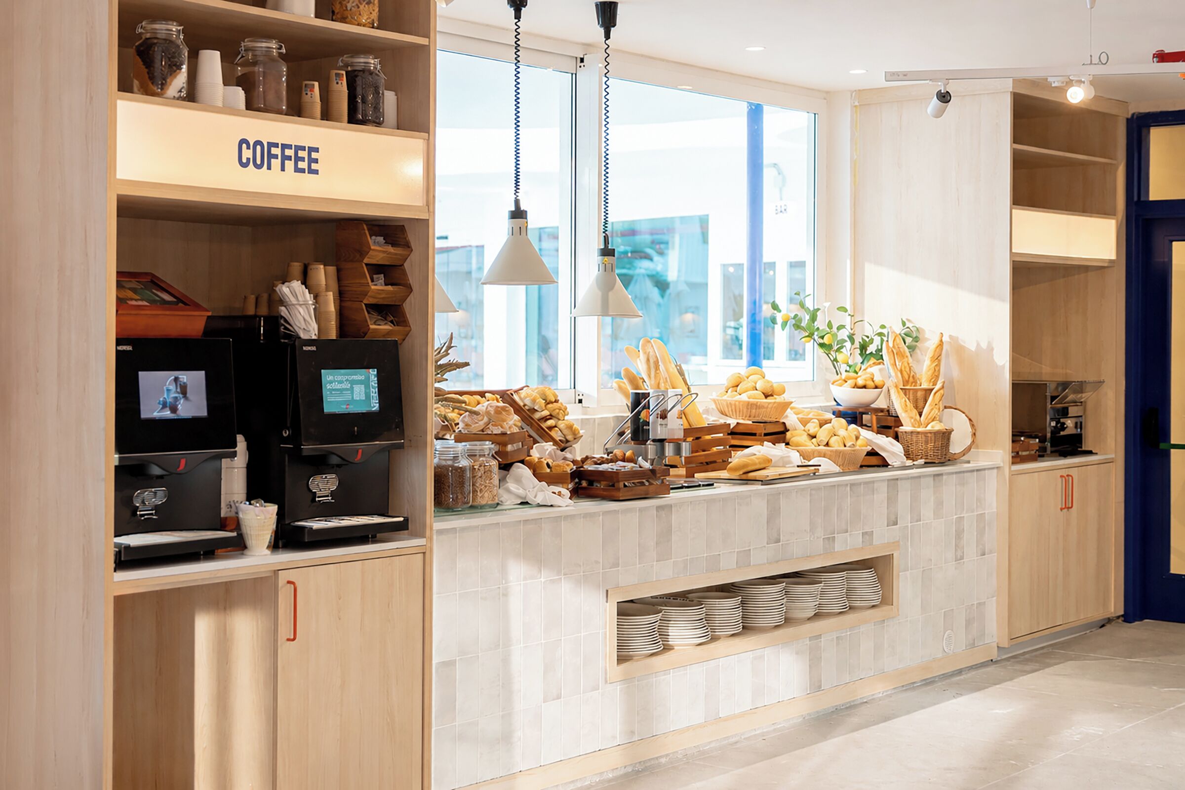 Una estación de café moderna con una máquina de café, una pantalla digital y una variedad de pasteles y pan.