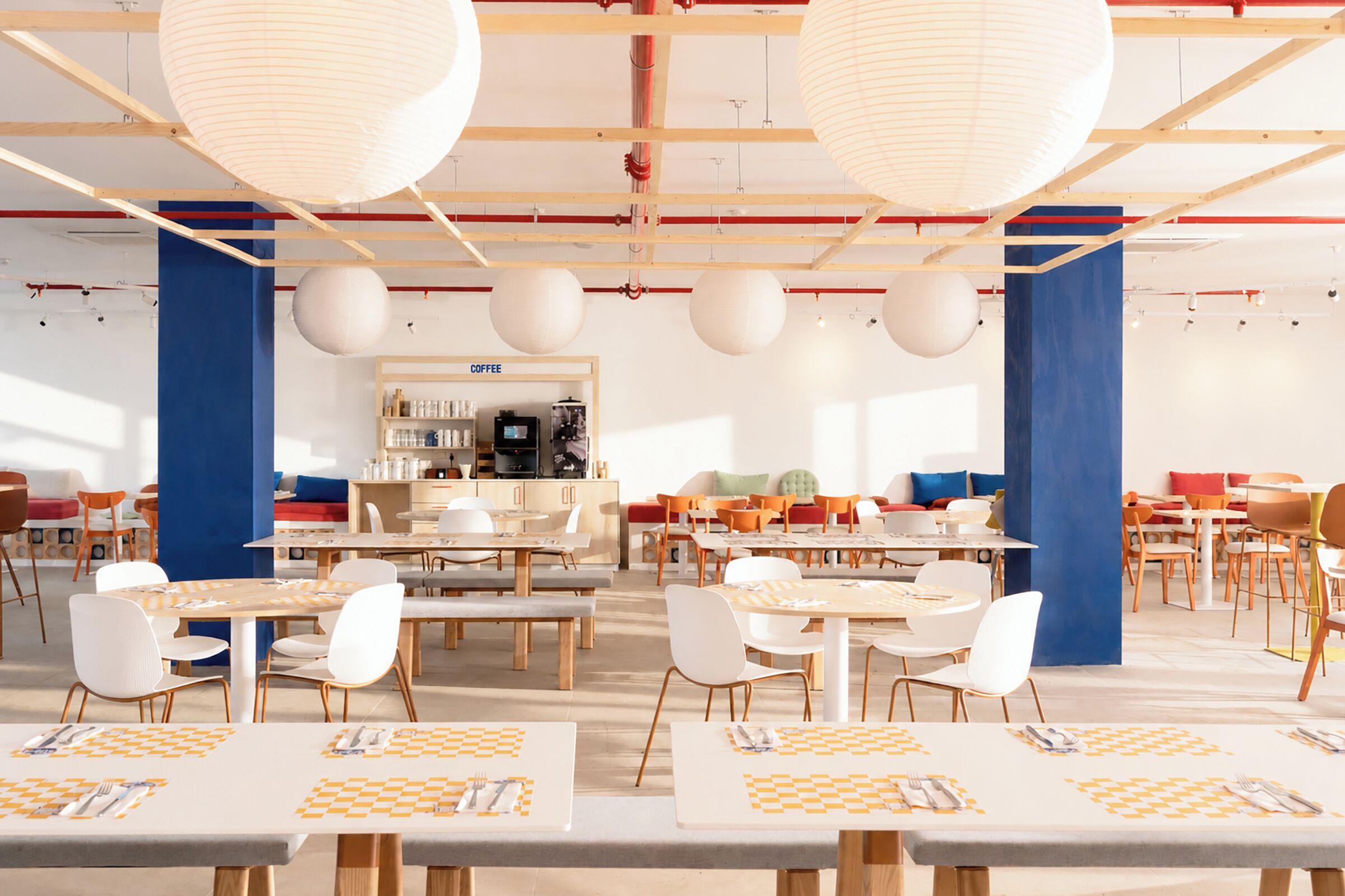 A modern dining area with multiple tables, chairs, and hanging paper lanterns.