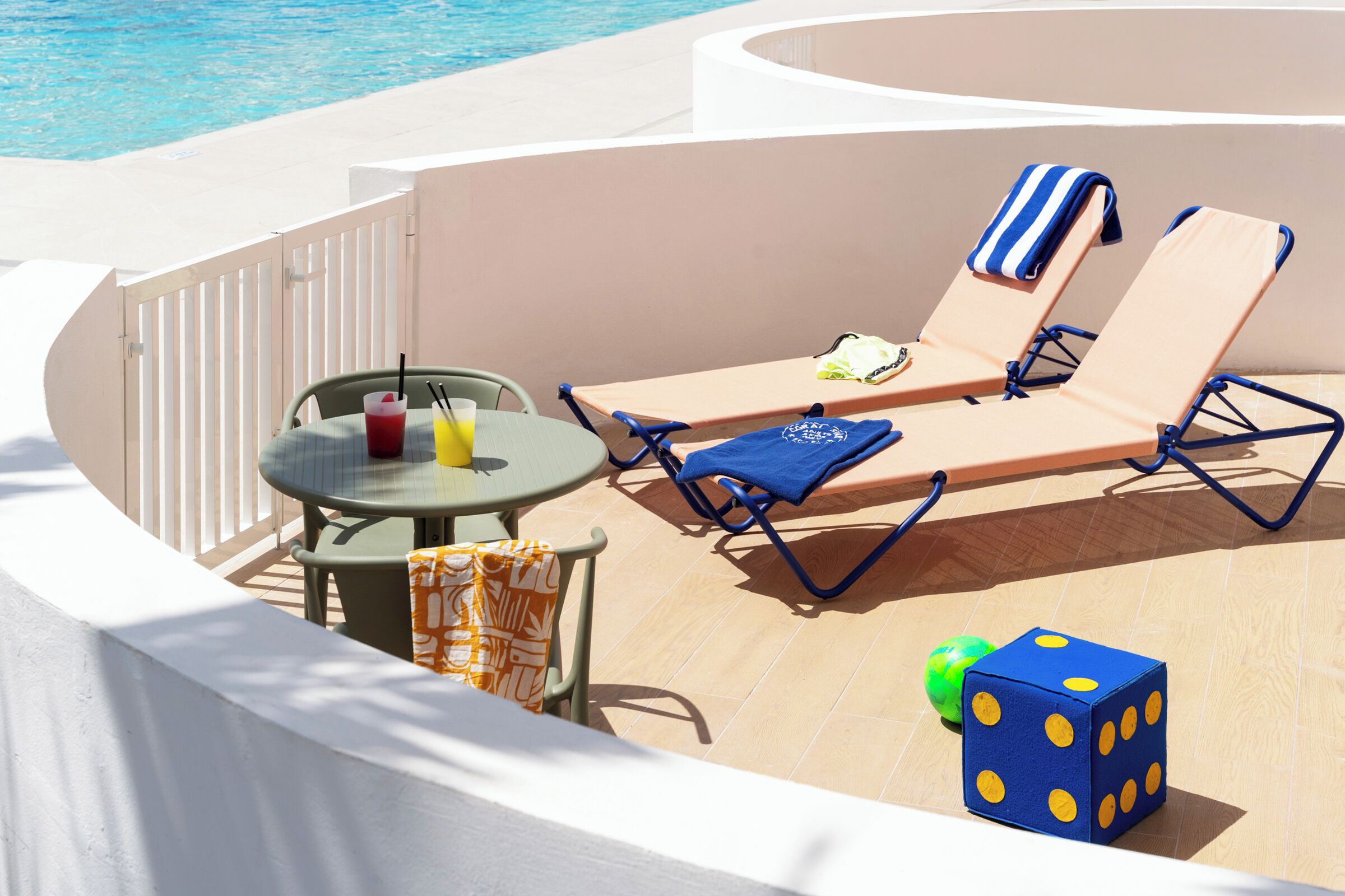 A sun lounge area with a pool view, a table with drinks, and a dice game.