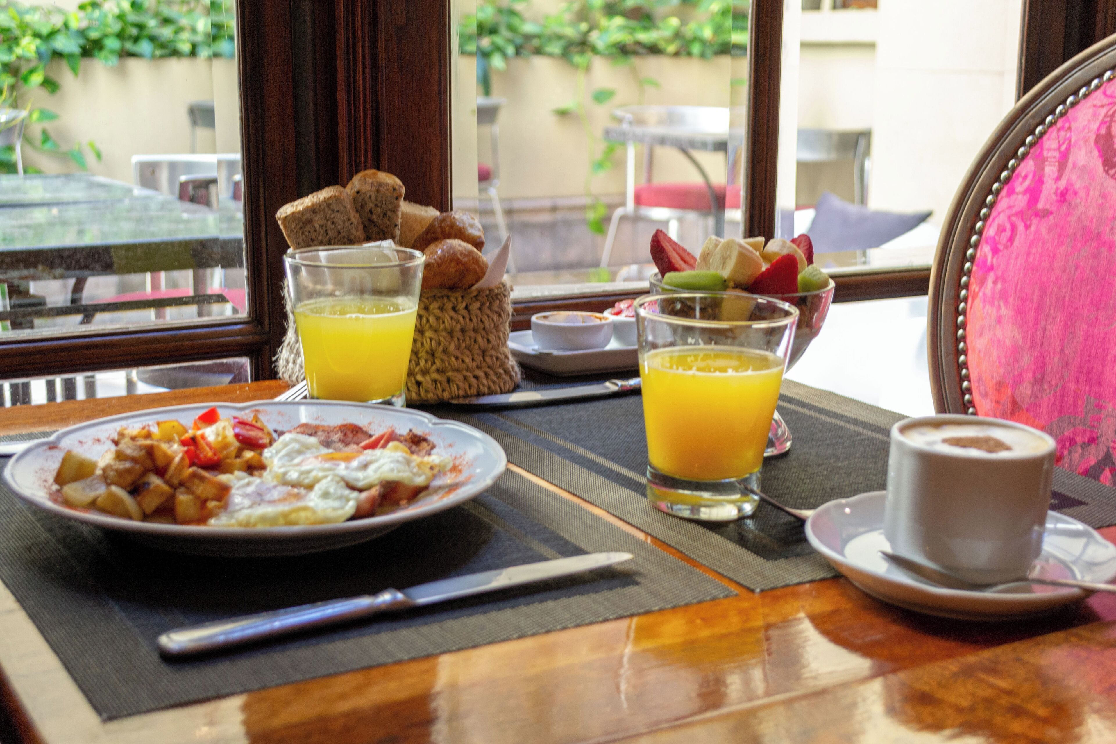 A breakfast table with plates of food, glasses of orange juice, and a cup of coffee.