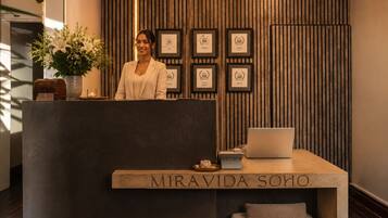 Un mostrador de recepción con un letrero que dice 'MIRAVIDA SOHO', un certificado enmarcado en la pared y una computadora portátil sobre la mesa.