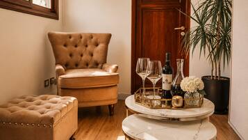 A room with a tufted armchair, ottoman, and a marble table with a tray holding wine glasses, bottles, and flowers.