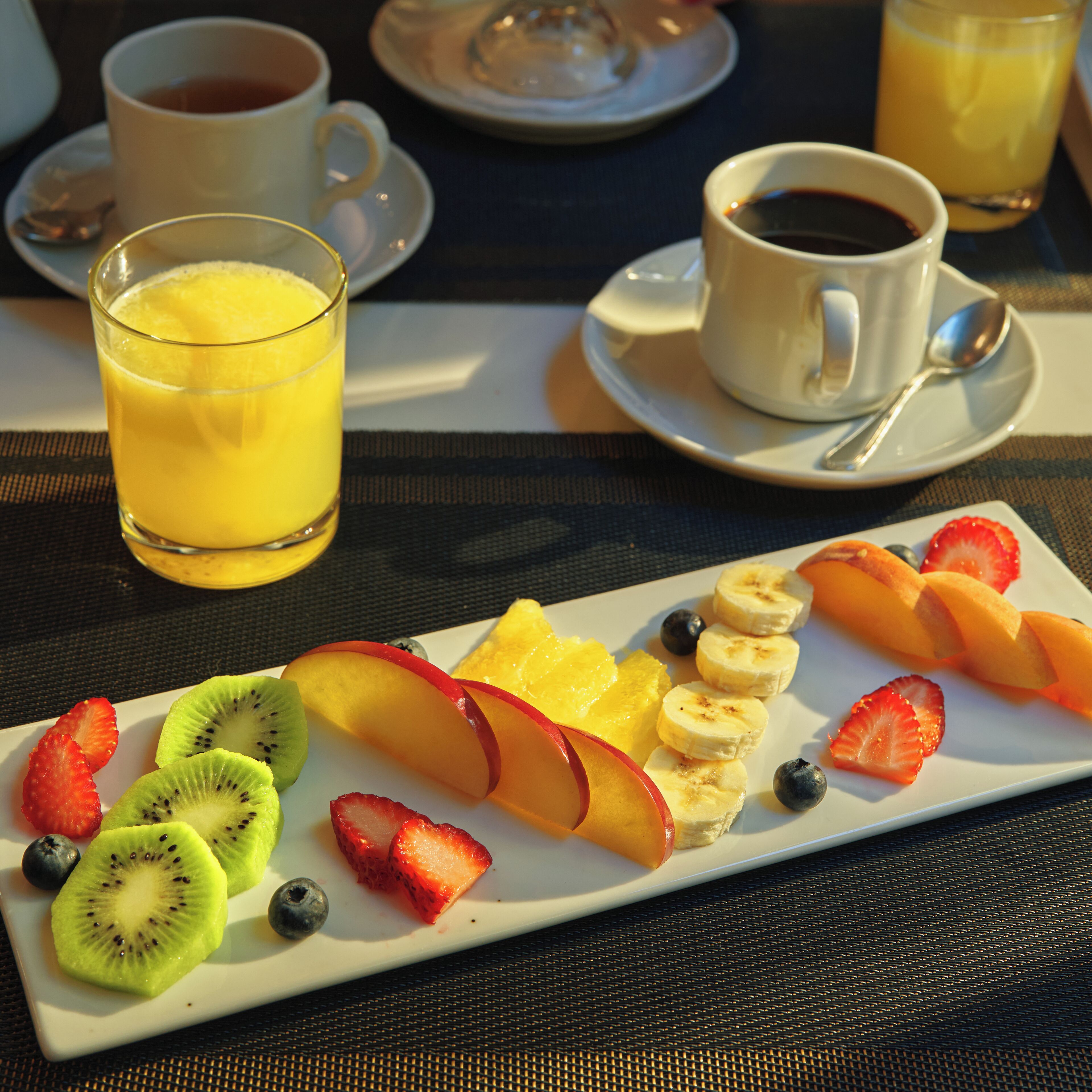 A breakfast setting with a fruit platter, a glass of orange juice, and two cups of coffee on a table.