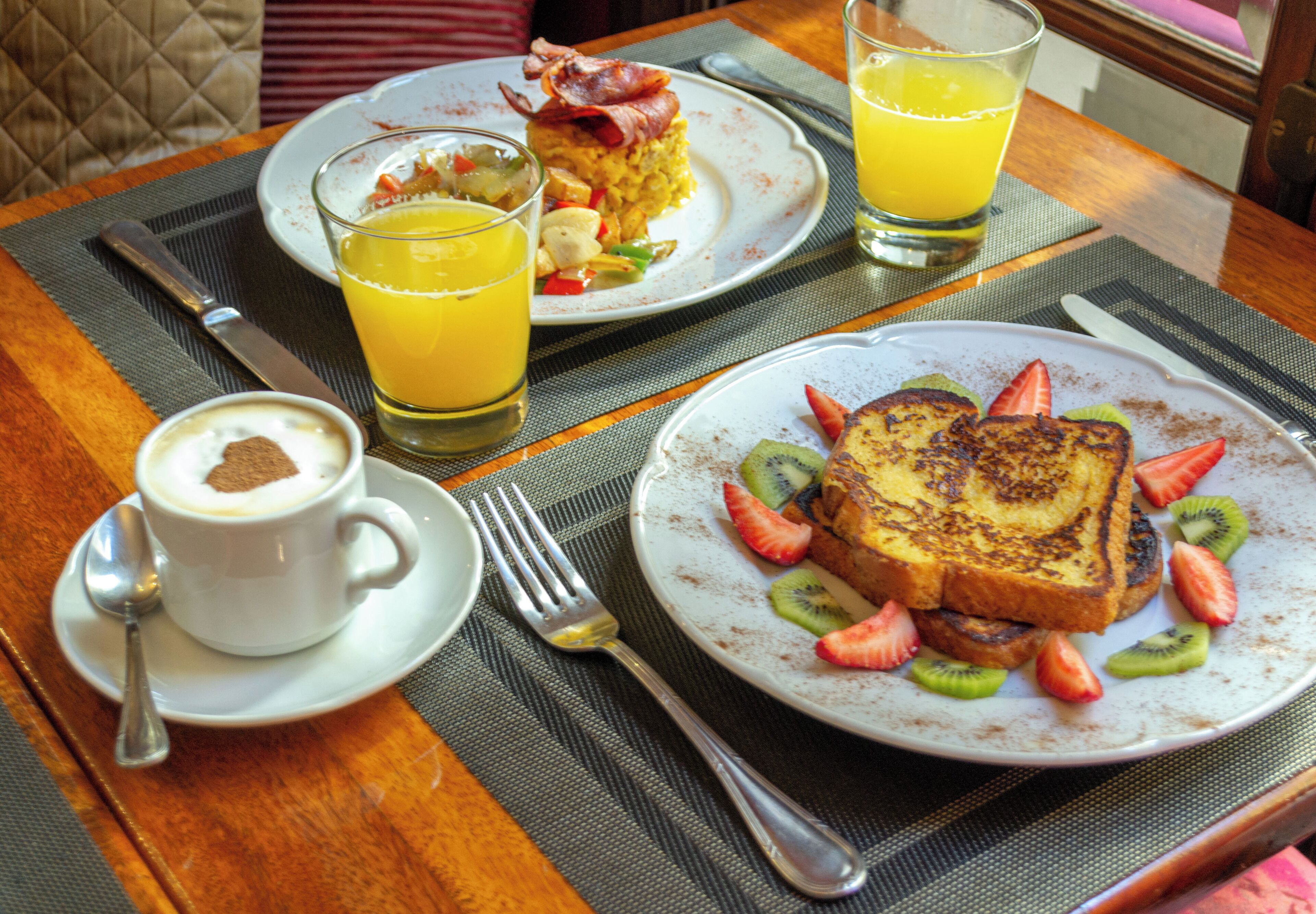 A breakfast setting with plates of toast, fruit, and orange juice.