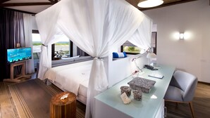 Une chambre à coucher avec un lit à baldaquin, un bureau avec une lampe, une chaise et un téléviseur posé sur un meuble.
