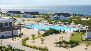 Un complexe hôtelier proposant plusieurs types d’hébergements en style bungalow, une piscine centrale dotée de chaises longues et offrant une vue sur l’océan.