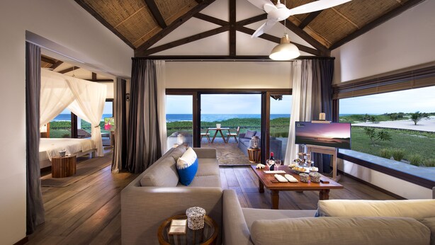 Un vaste espace de vie comprenant un grand canapé, une table basse et un téléviseur. Un balcon offre une vue sur l’océan.