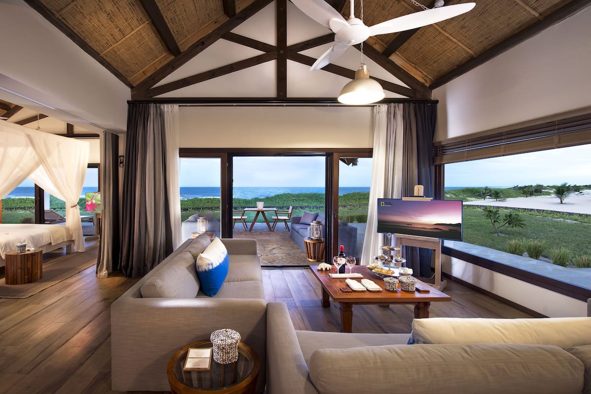 Amplia sala de estar con un sofá grande, una mesa de centro y un televisor. Hay un balcón con vistas al océano.