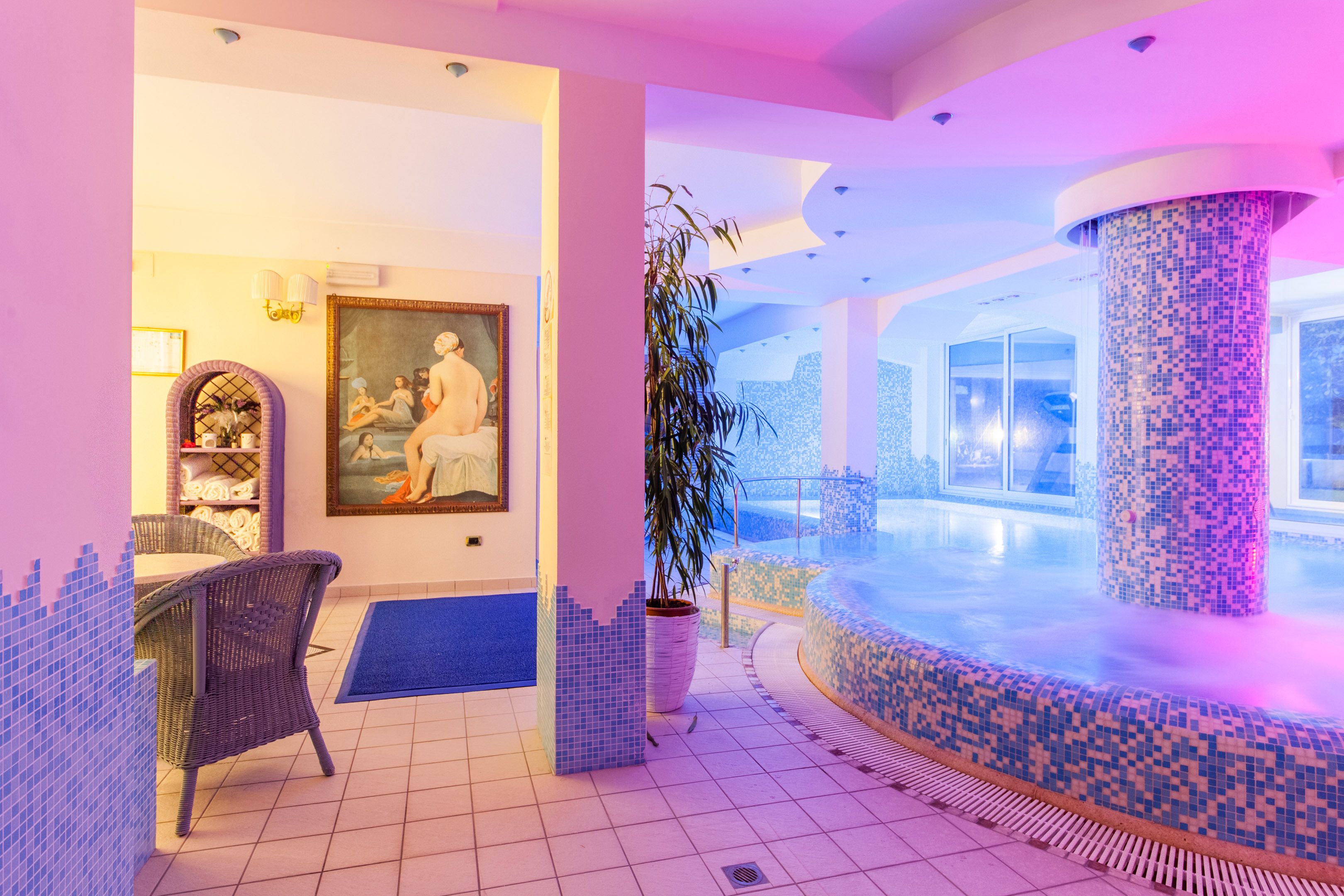Un área de spa con piscina de mosaicos, mobiliario de mimbre y un cuadro grande en la pared.