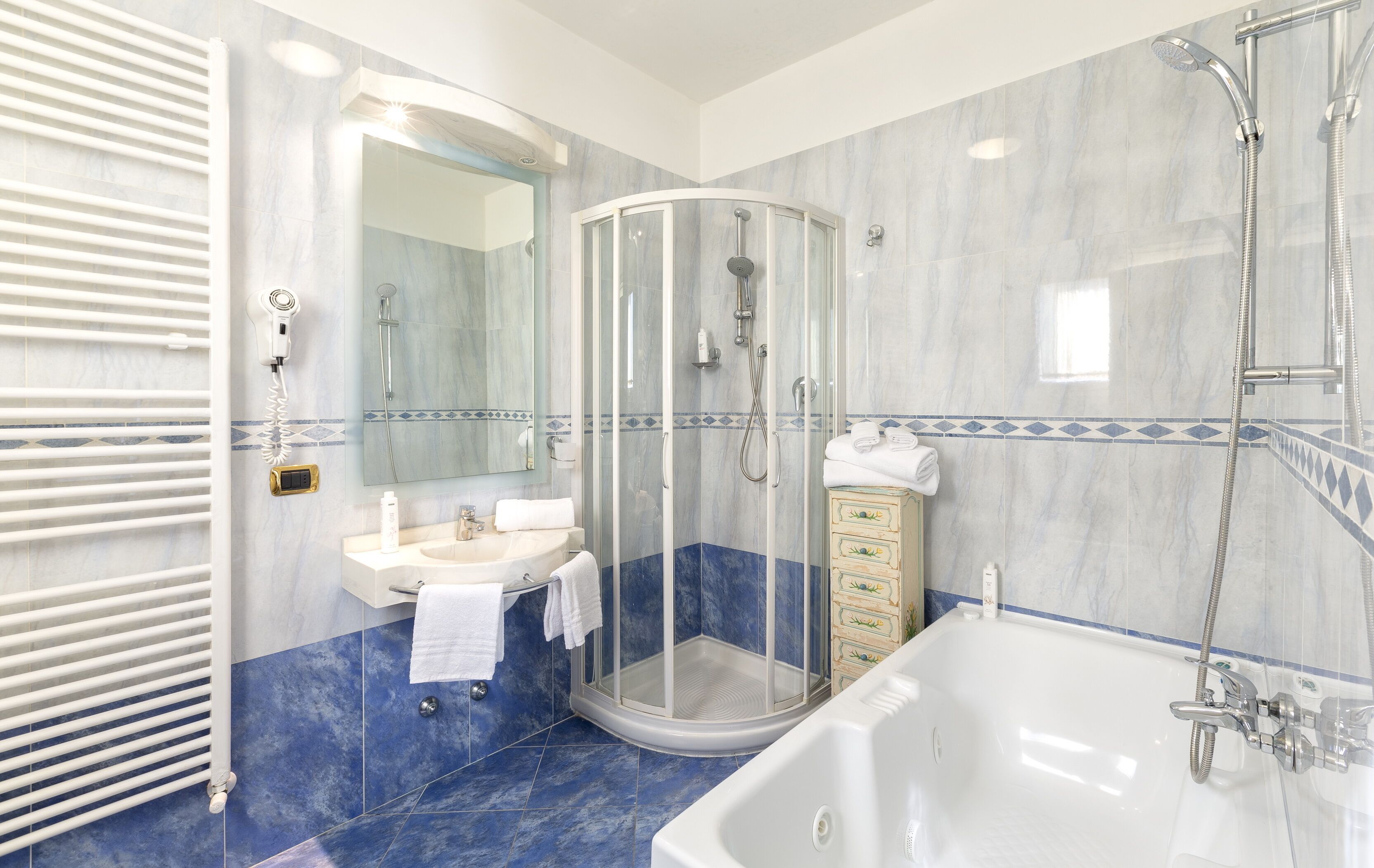 A modern bathroom with a glass-enclosed shower, a bathtub, a sink, and a vanity with drawers.