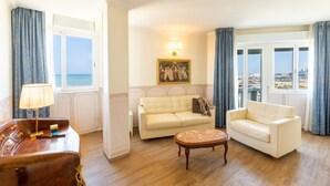 A room with a sofa, a chair, a small table, and a lamp. There is a painting on the wall and a window with curtains. - Hotel Baia Imperiale & Spa (Rimini)