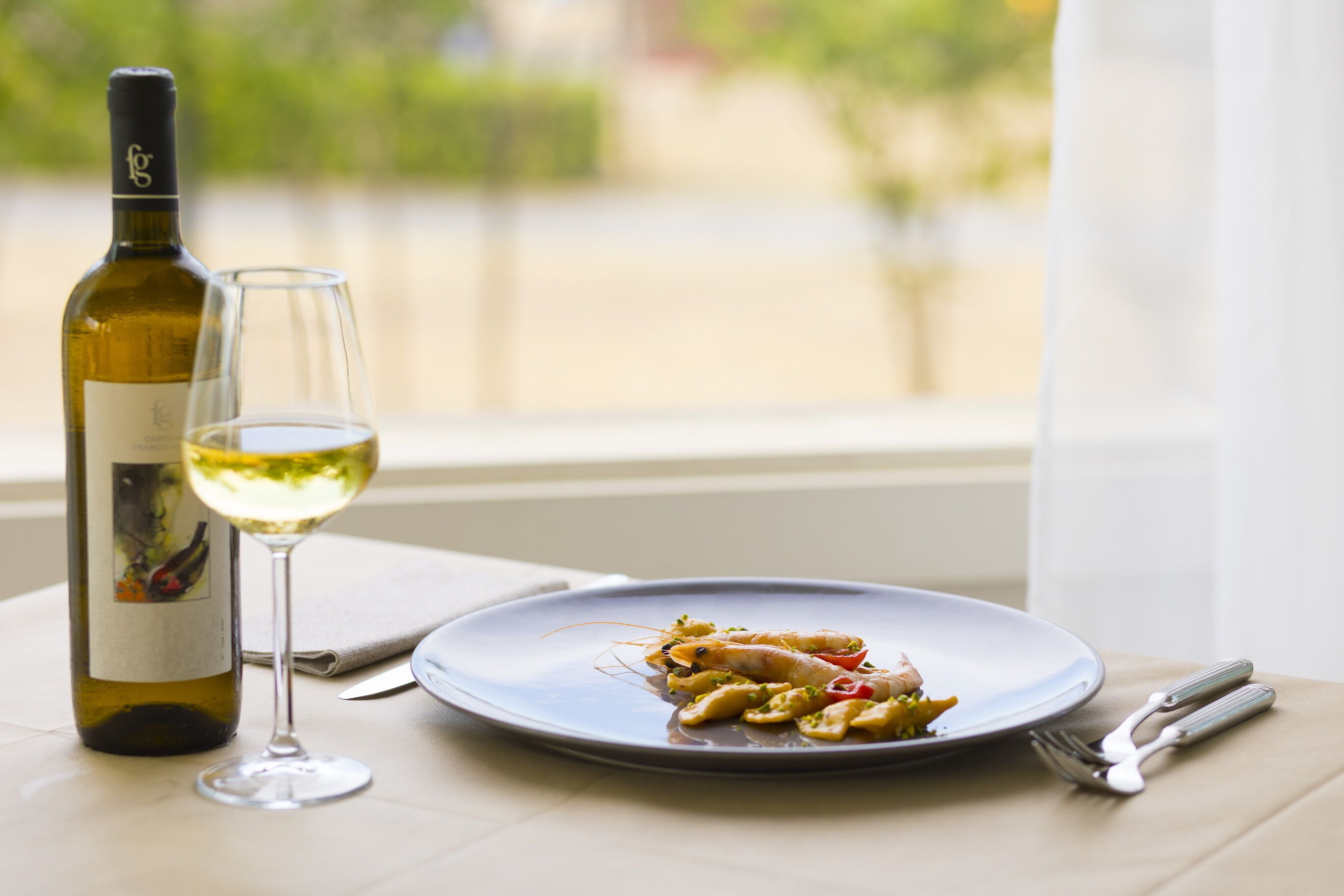 Un tavolo con una bottiglia di vino, un bicchiere e un piatto di cibo.