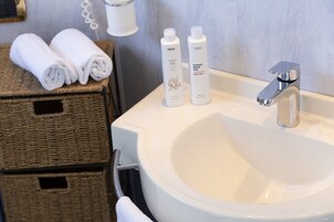 Un bagno con un lavandino bianco, due articoli da toilette sul piano e un asciugamano in un cesto di vimini.