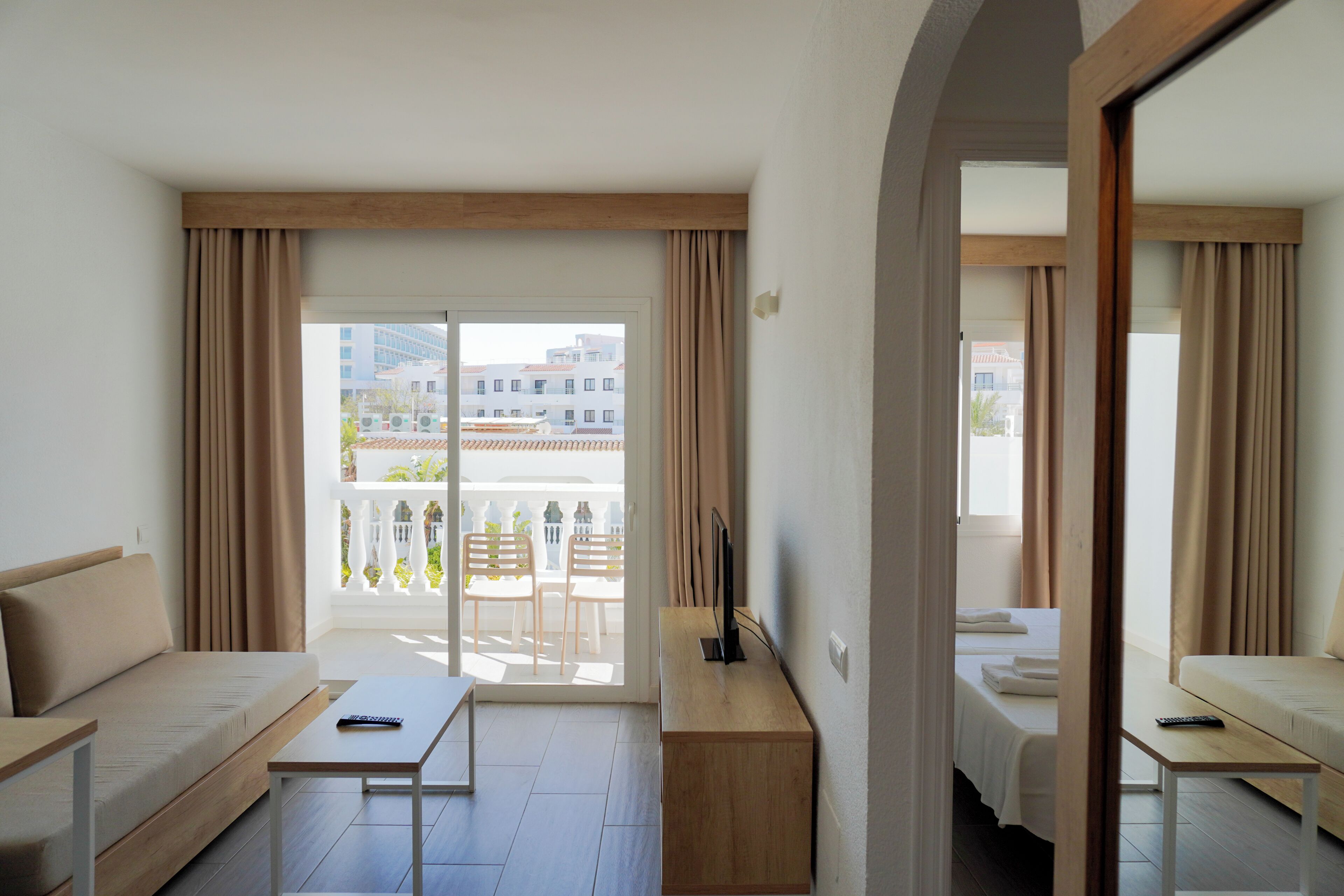 Une chambre d’hôtel avec un canapé, une petite table, une télévision et un balcon donnant sur des immeubles.