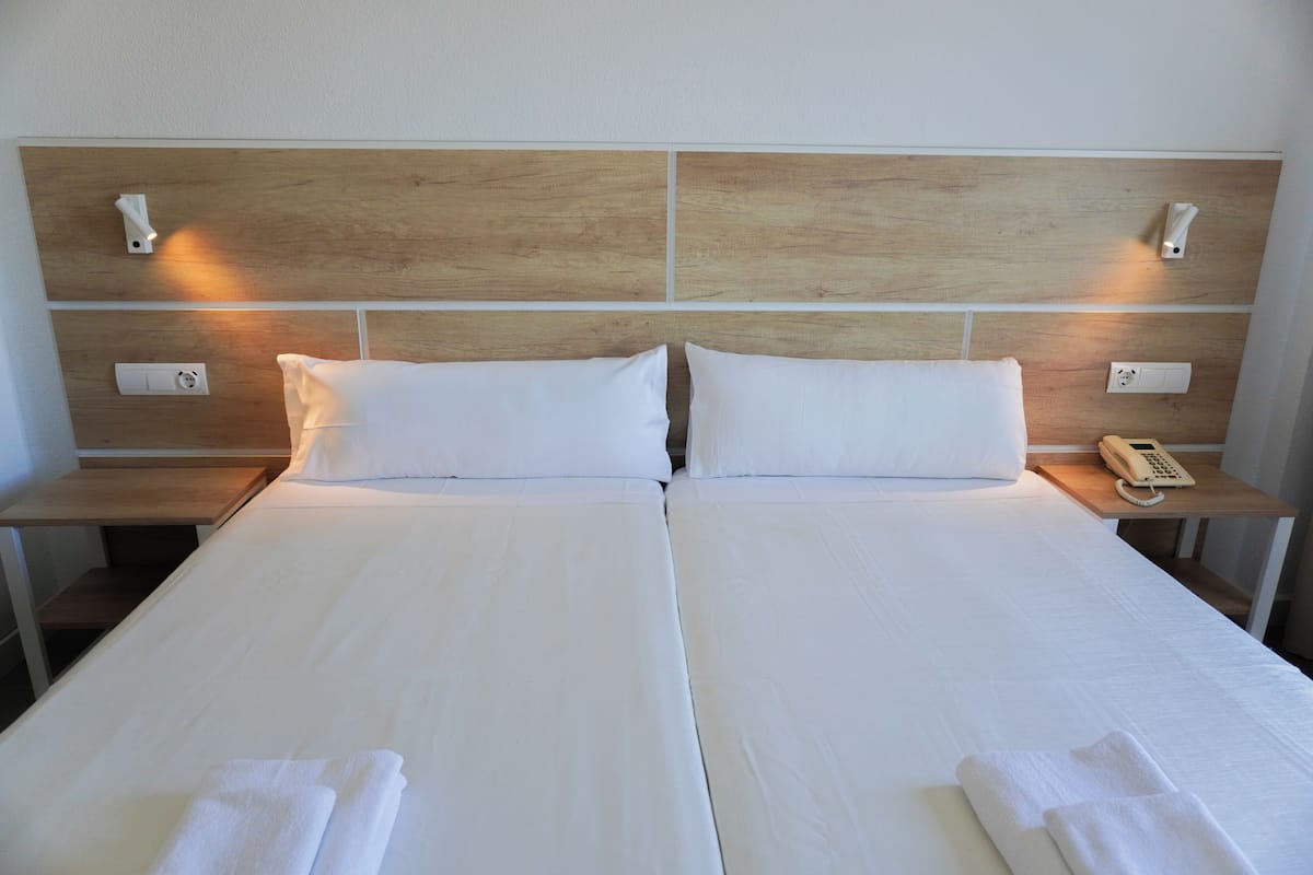 A double bed with white linens, two bedside tables with lamps, and a wooden headboard.