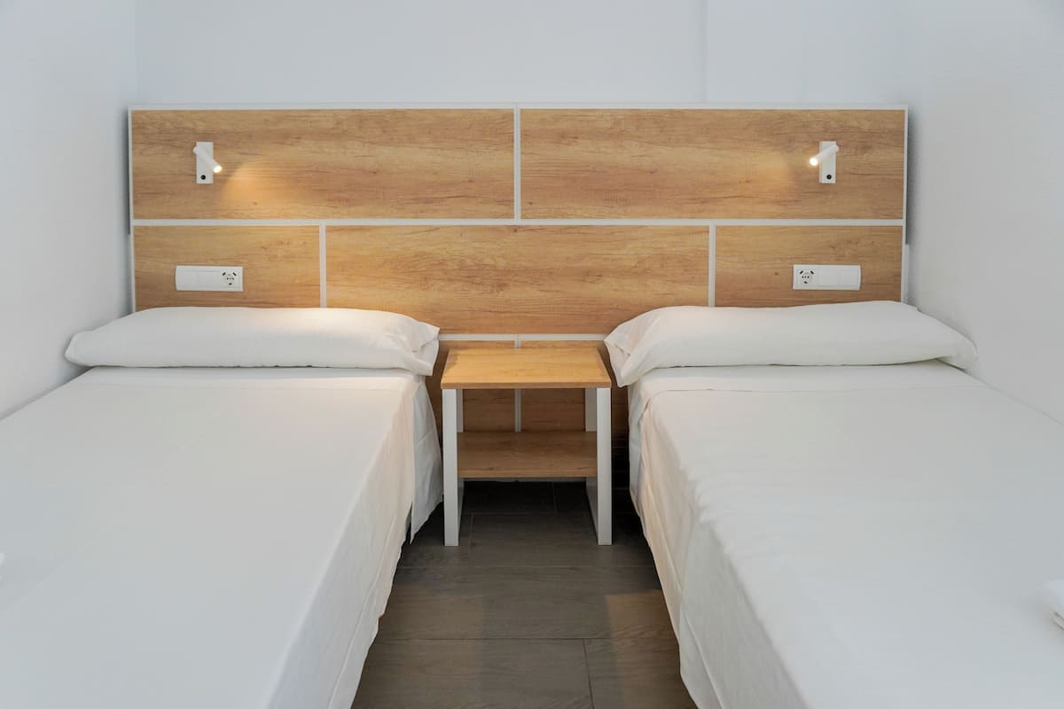 A room with two single beds, a wooden headboard, bedside lamps, and a small wooden table.