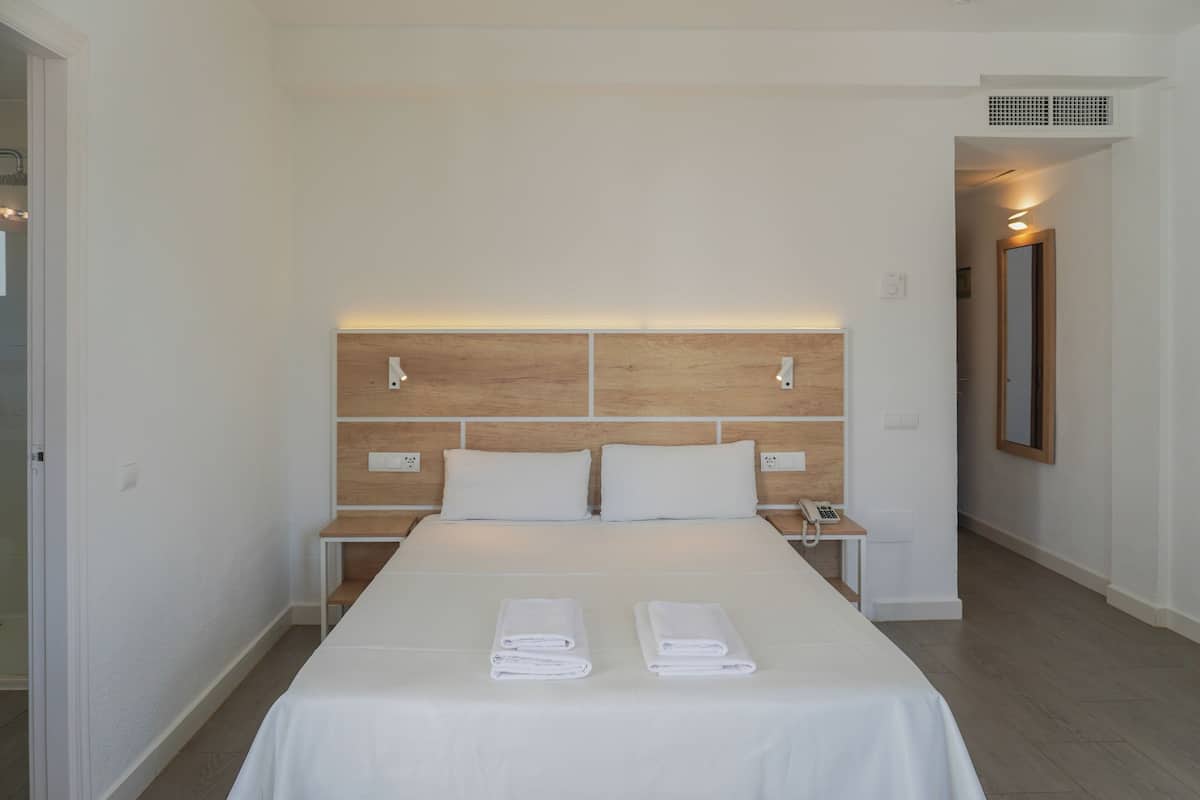 A hotel room with a large bed, two bedside tables, a wooden headboard, and two neatly folded towels on the bed.