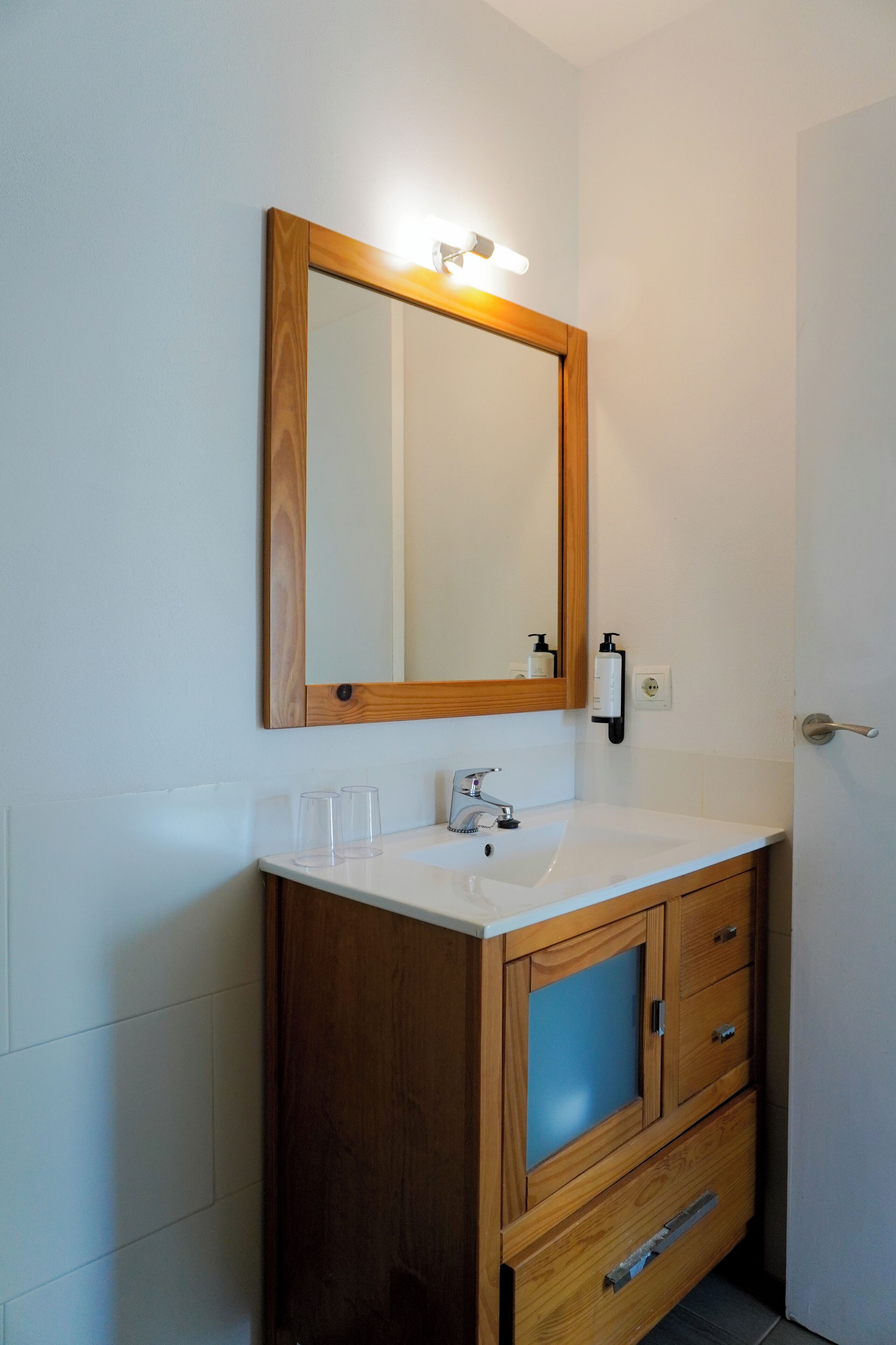 Une salle de bain avec un meuble-lavabo en bois, un miroir avec éclairage intégré et un lavabo blanc.