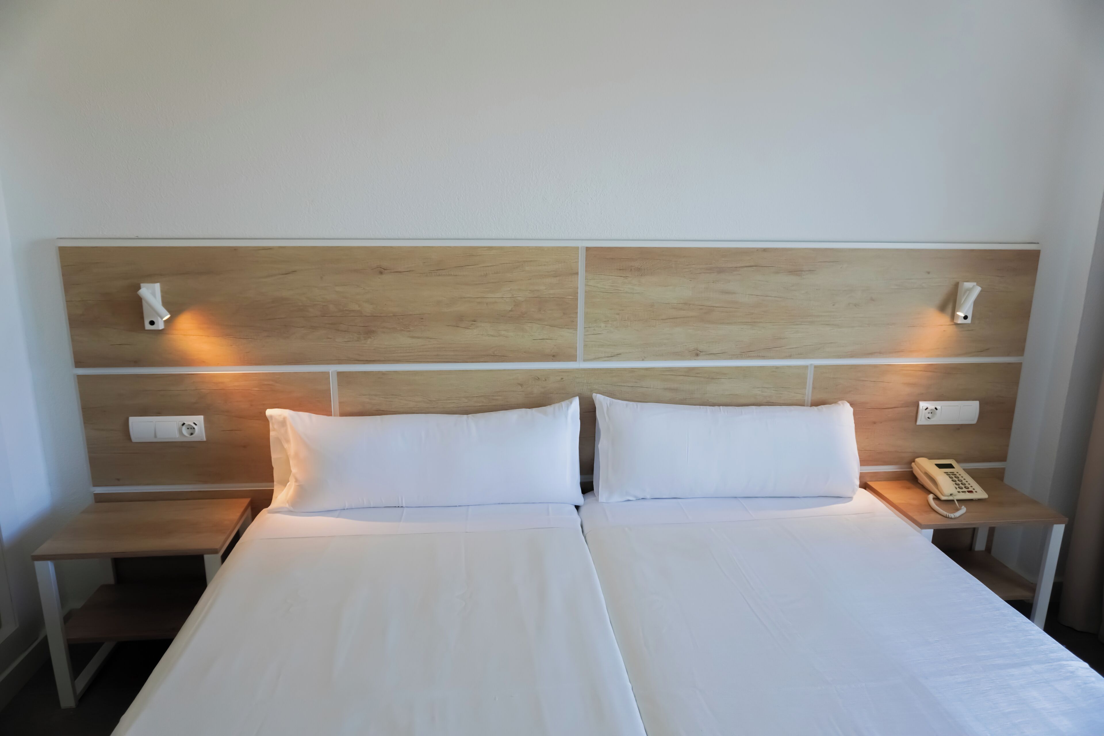 Un lit double avec du linge de lit blanc, deux tables de chevet avec des lampes et une tête de lit en bois.