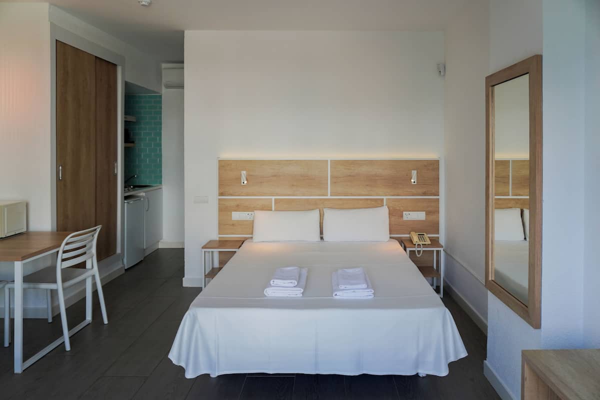A hotel room with a bed, a desk, a chair, a nightstand, and a mirror.